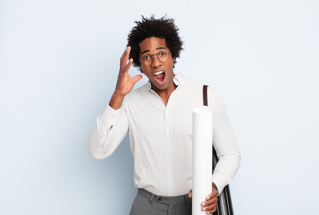 Giovane uomo afro nero che grida con le mani in alto, sentendosi furioso, frustrato, stressato e sconvolto