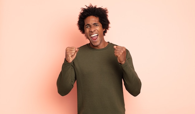 Photo young black afro man shouting aggressively with an angry expression or with fists clenched celebrating success