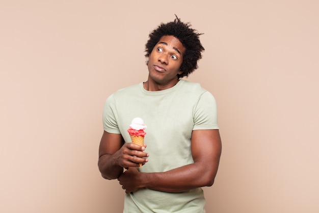 Young black afro man shrugging, feeling confused and uncertain, doubting with arms crossed and puzzled look