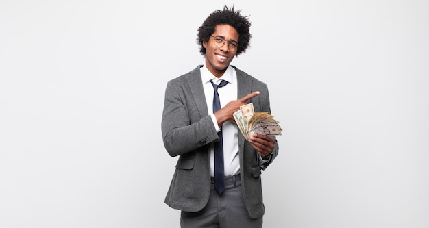 young black afro man smiling cheerfully, feeling happy and pointing to the side and upwards, showing object in copy space