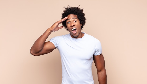 Young black afro man smiling, feeling carefree, relaxed and happy, dancing and listening to music, having fun at a party