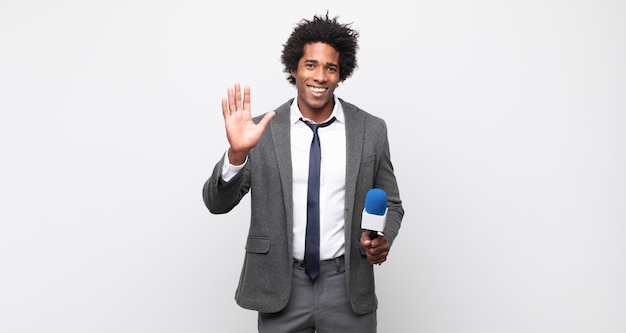 Young black afro man smiling happily and cheerfully, waving hand, welcoming and greeting you, or saying goodbye