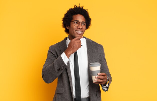 Giovane uomo afro nero che sorride felicemente e sogna ad occhi aperti o dubita, guardando di lato