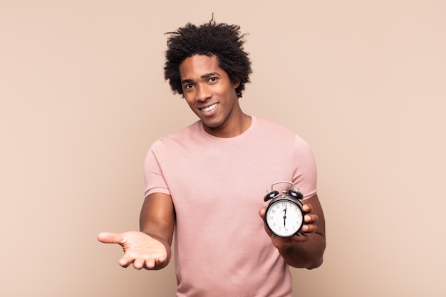 Giovane uomo afro nero che sorride felicemente con sguardo amichevole, fiducioso, positivo, offrendo e mostrando un oggetto o un concetto