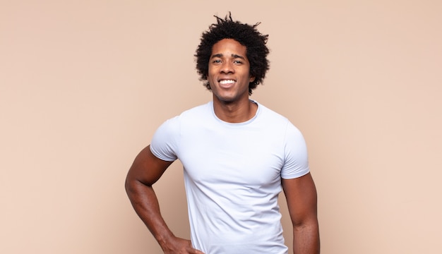 Young black afro man smiling happily with a hand on hip and confident, positive, proud and friendly attitude