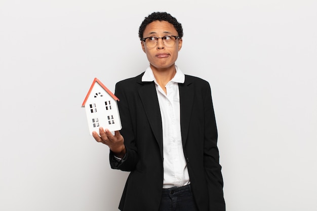 Young black afro woman looking puzzled and confused, biting lip with a nervous gesture, not knowing the answer to the problem