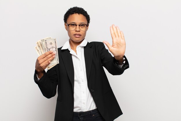 Young black afro woman looking serious, stern, displeased and angry showing open palm making stop gesture