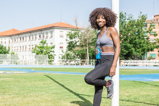 young black athlete woman with afro hair standing smiling looking at camera with isotonic drink