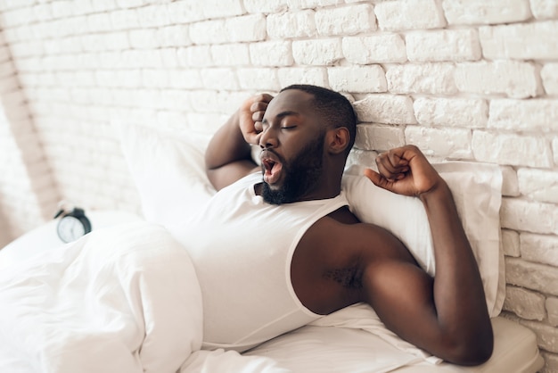 Young black, awakened man is stretched out in bed.