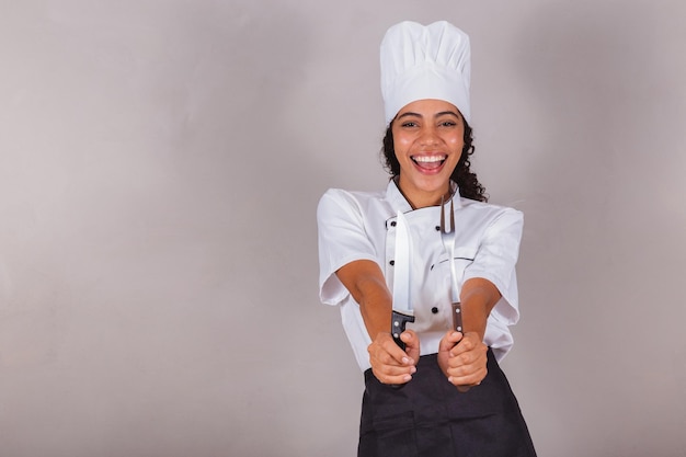 Foto giovane cuoca brasiliana nera che tiene coltello e forchetta per preparare il barbecue di carne