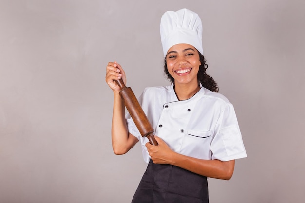 Photo young black brazilian woman cook holding wooden rolling pin for preparing pasta pizza and bread