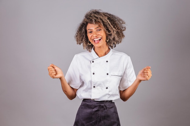 Young black Brazilian woman cook masterchef wearing restaurant uniform celebrating extremely happy