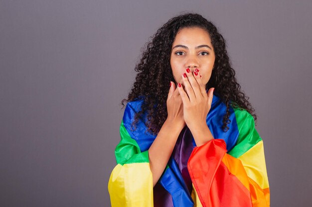 Young black brazilian woman covering her mouth militancy with\
lgbt flag diversity fight against prejudice