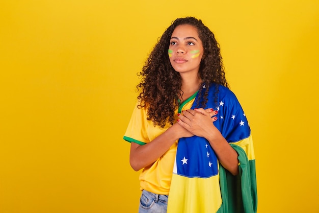 Young black brazilian woman soccer fan with brazil flag singing the national anthem