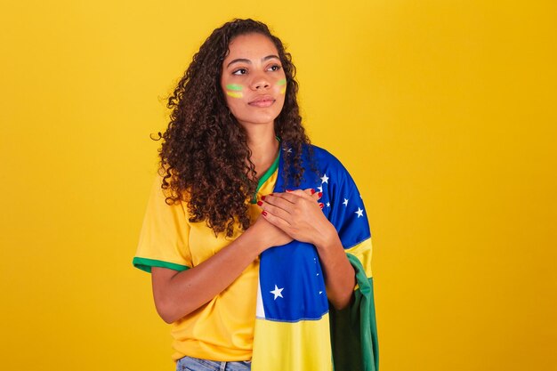 Фото Молодая чернокожая бразильская футбольная фанатка с бразильским флагом поет национальный гимн