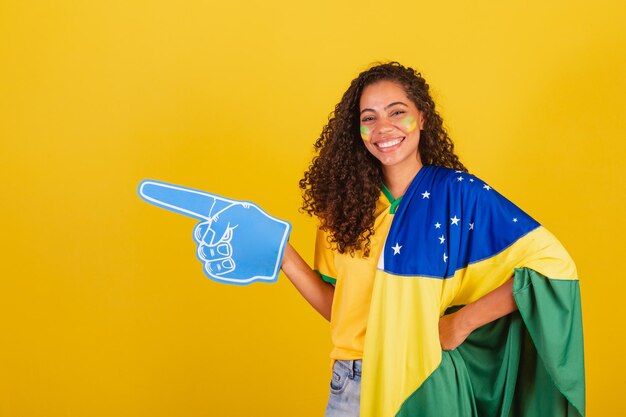Young black brazilian woman soccer fan with foam finger pointing to the left