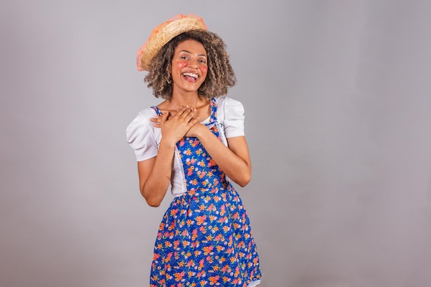 Young black Brazilian woman with country clothes dressed for Festa Junina Saint John's festival in love hands on heart hope