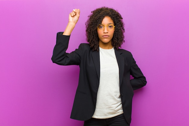 Young black business woman feeling serious, strong and rebellious, raising fist up, protesting or fighting for revolution