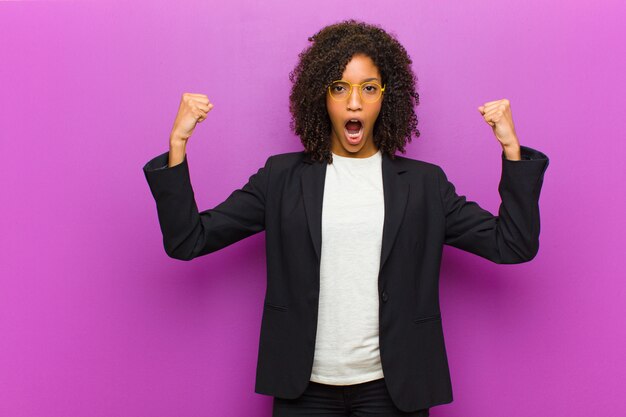 Young black business woman shouting aggressively with an angry expression or with fists clenched celebrating success