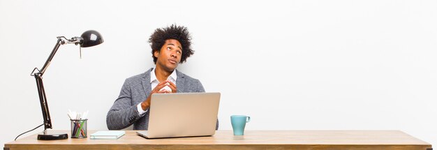 Young black businessman scheming and conspiring, thinking devious tricks and cheats, cunning and betraying on a desk