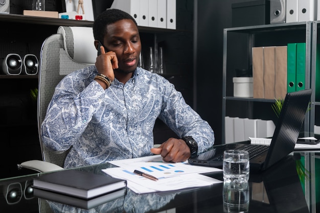 Young black businessman talking on mobile phone sitting at computer Desk in office