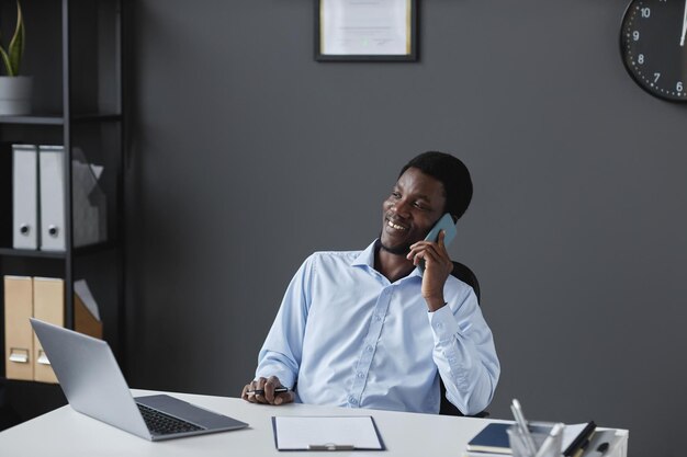 Young black businessman talking on phone and sitting at workplace desk in office