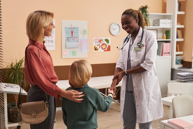 Молодой чернокожий врач в качестве педиатра приветствует семью в детской клинике