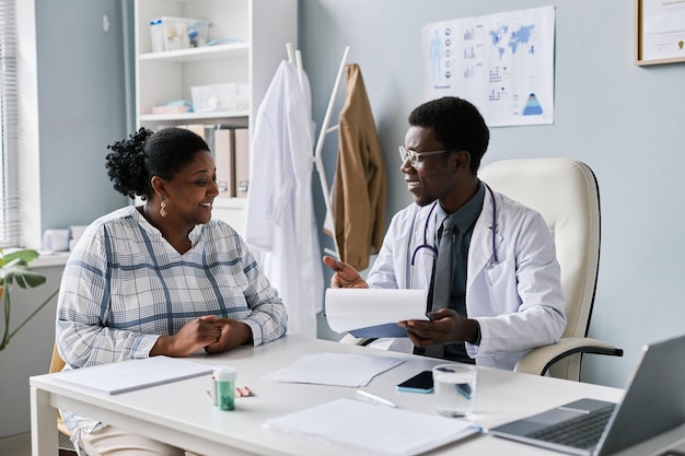 Young black doctor talking to young woman during consultation in clinic smiling