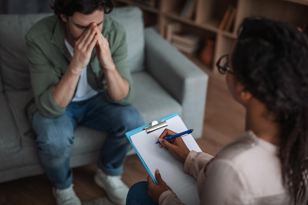 Photo young black female psychologist consults unhappy european man in clinic interior unrecognizable