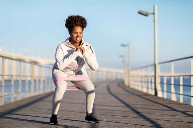 Молодая черная женщина в спортивной одежде тренируется с петлей сопротивления на открытом воздухе