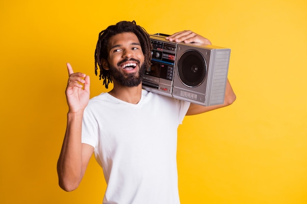 Young black guy raise finger up look empty space hold vintage recorder open mouth wear white t-shirt isolated yellow color background