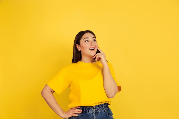 Young black-haired woman in yellow T-shirt against yellow wall
