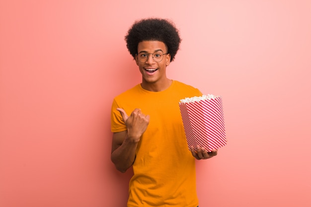 Young black holding a popcorn bucket surprised, feels successful and prosperous