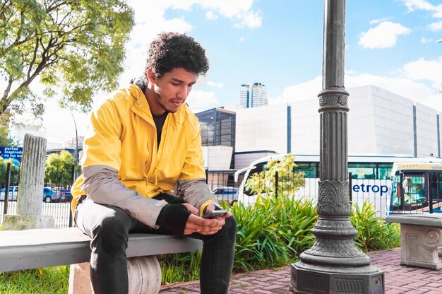 Young black latino man dressed in yellow sitting in an urban plaza in the daytime with his phone