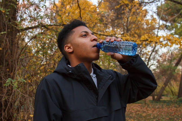 Young black man drinking water from a plastic bottle in the field.