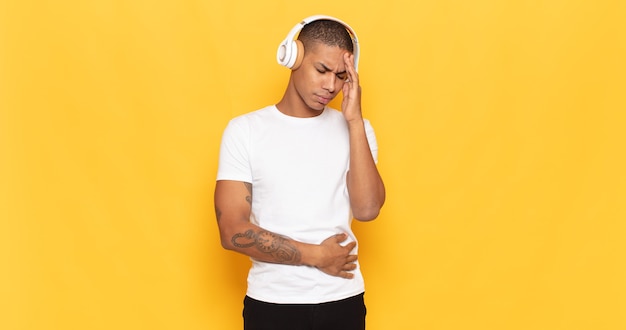 Young black man feeling bored, frustrated and sleepy after a tiresome, dull and tedious task, holding face with hand