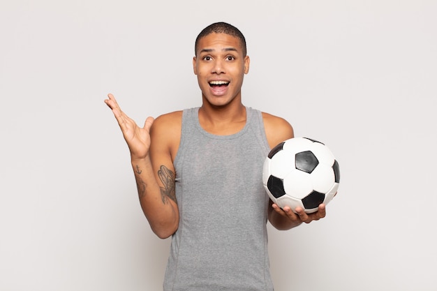 Young black man feeling happy, excited, surprised or shocked, smiling and astonished at something unbelievable