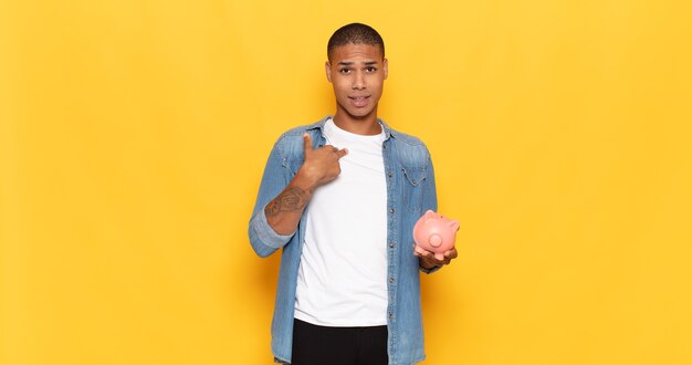 Young black man feeling happy, surprised and proud, pointing to self with an excited, amazed look