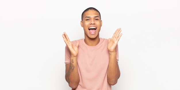 Young black man feeling shocked and excited, laughing, amazed and happy because of an unexpected surprise