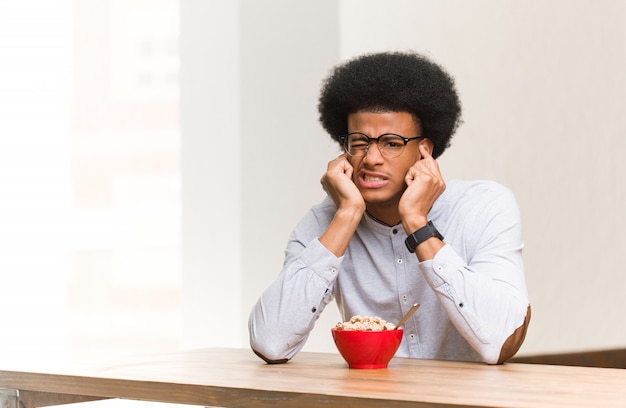 Young black man having a breakfast covering ears with hands