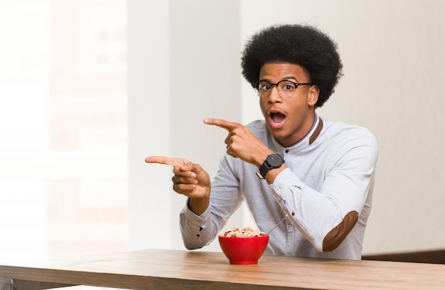 Young black man having a breakfast pointing to the side with finger