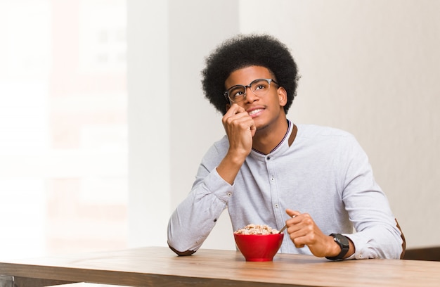 Il giovane uomo di colore che mangia una prima colazione si è disteso pensando a qualcosa che esamina uno spazio della copia