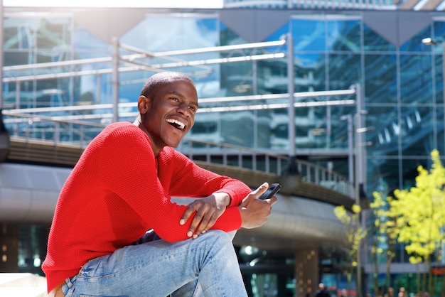 young black man laughing in the city with mobile phone