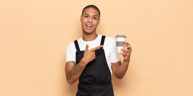 Young black man looking excited and surprised pointing to the side and upwards to copy space