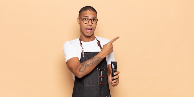 Young black man looking excited and surprised pointing to the side and upwards to copy space