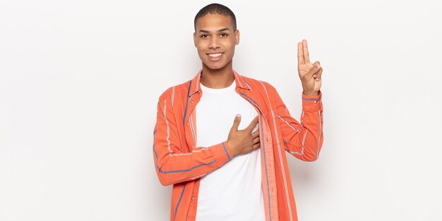 Young black man looking happy, confident and trustworthy, smiling and showing victory sign, with a positive attitude