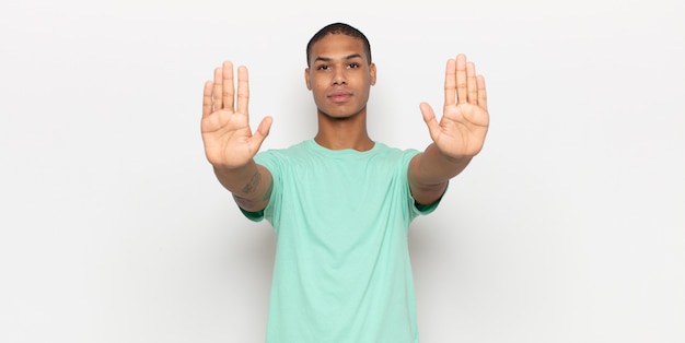 Young black man looking serious, unhappy, angry and displeased forbidding entry or saying stop with both open palms