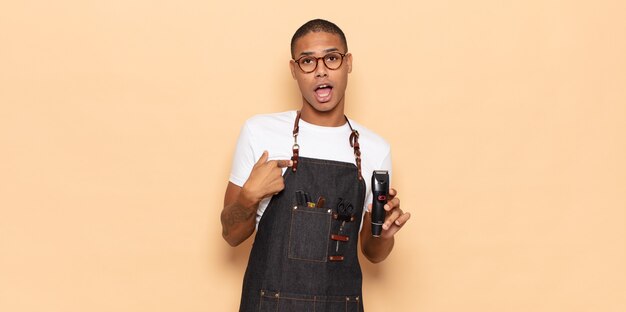 Young black man looking shocked and surprised with mouth wide open, pointing to self