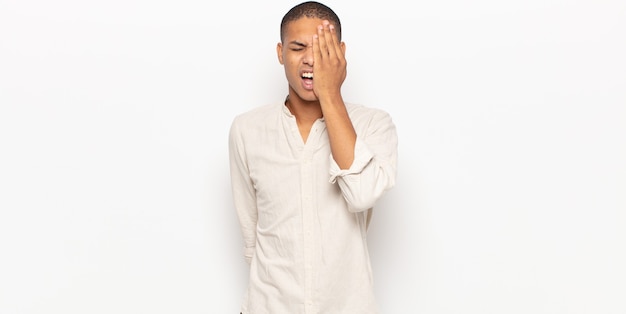 Young black man looking sleepy, bored and yawning, with a headache and one hand covering half the face