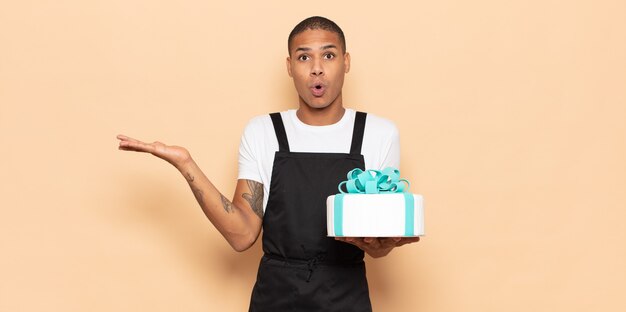 Young black man looking surprised and shocked, with jaw dropped holding an object with an open hand on the side